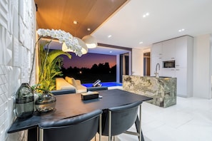 A modern kitchen with a built-in microwave and a stone island. There is a dining area with a table and chairs, and a view of the ocean at sunset.