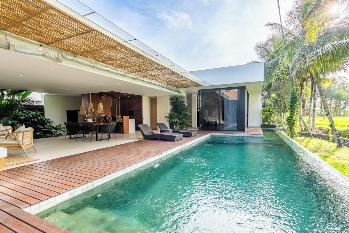 A modern outdoor pool area with a wooden deck, lounge chairs, and a dining setup.