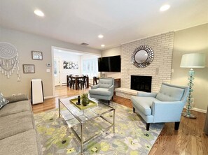 A living room with a fireplace, two armchairs, a coffee table, and a TV mounted on the wall.