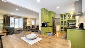 Una cocina moderna con gabinetes verdes, una mesa de comedor con un tazón, y una zona de estar con un sofá y una ventana.