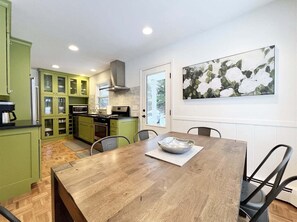 A kitchen with green cabinets, a wooden dining table, and a painting of flowers.