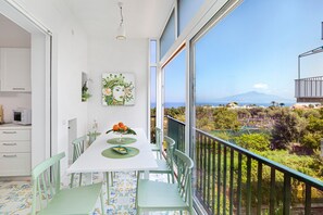 A dining area with a table set for two, a view of the outdoors, and a balcony with a railing. - Estate4home- Casa Maridea (Sorrento)
