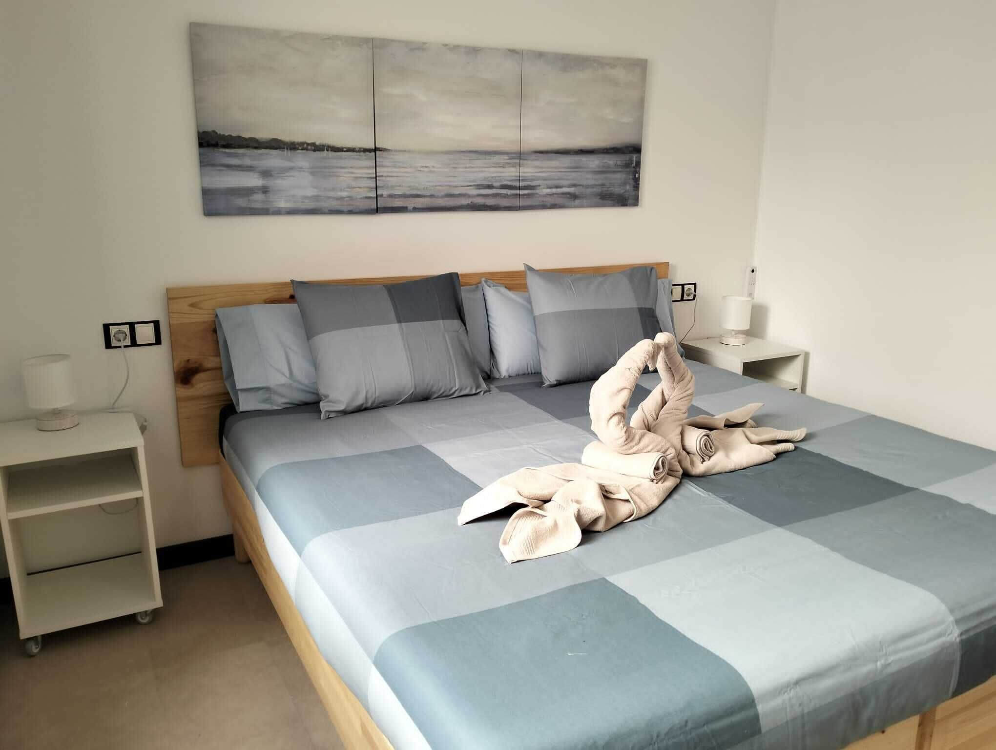 Een net opgemaakt bed met een geruit sprei, een houten hoofdbord en een aan de muur hangend landschapsschilderij.
