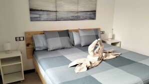 A neatly made bed with a checkered bedspread, a wooden headboard, and a wall-mounted painting of a landscape. - Beachfront apartment, with sea and pool view, in El Cotillo, Fuerteventura (El Cotillo, La Oliva)