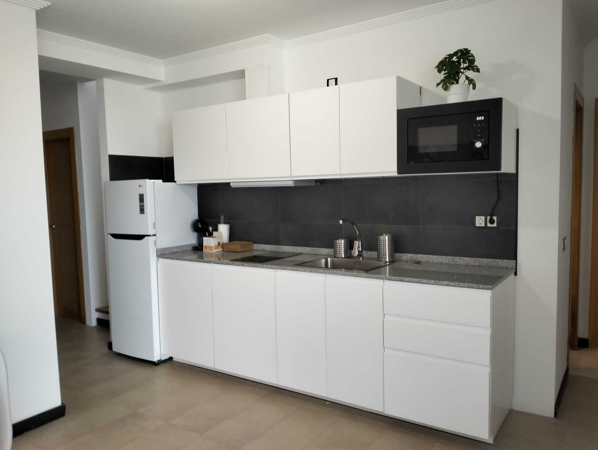 A modern kitchen with white cabinetry, a built-in microwave, and a sink.