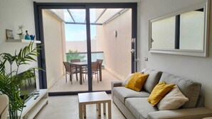 A modern living room with a grey sofa, yellow cushions, a small white table, and a dining area with chairs and a table. - Beachfront apartment, with sea and pool view, in El Cotillo, Fuerteventura (El Cotillo, La Oliva)