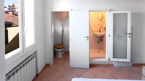 Un baño compacto con inodoro, bidé y lavamanos, con ventana y radiador.