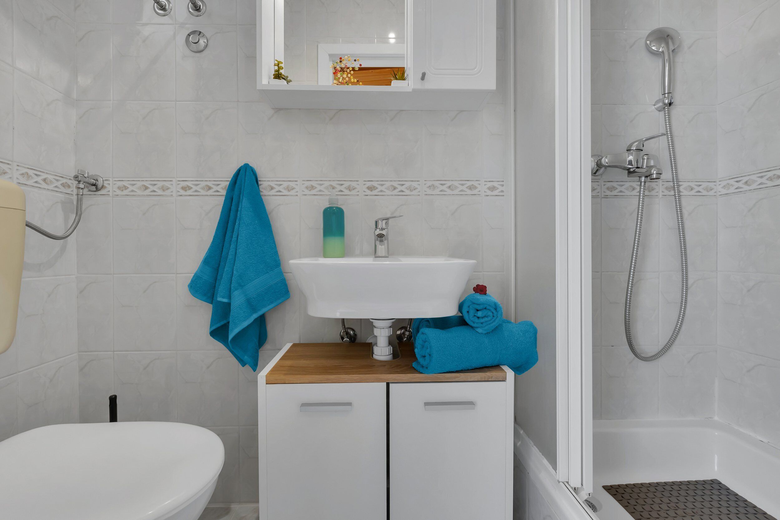 A bathroom with a white sink, a wooden cabinet, a towel rack, and a shower area.