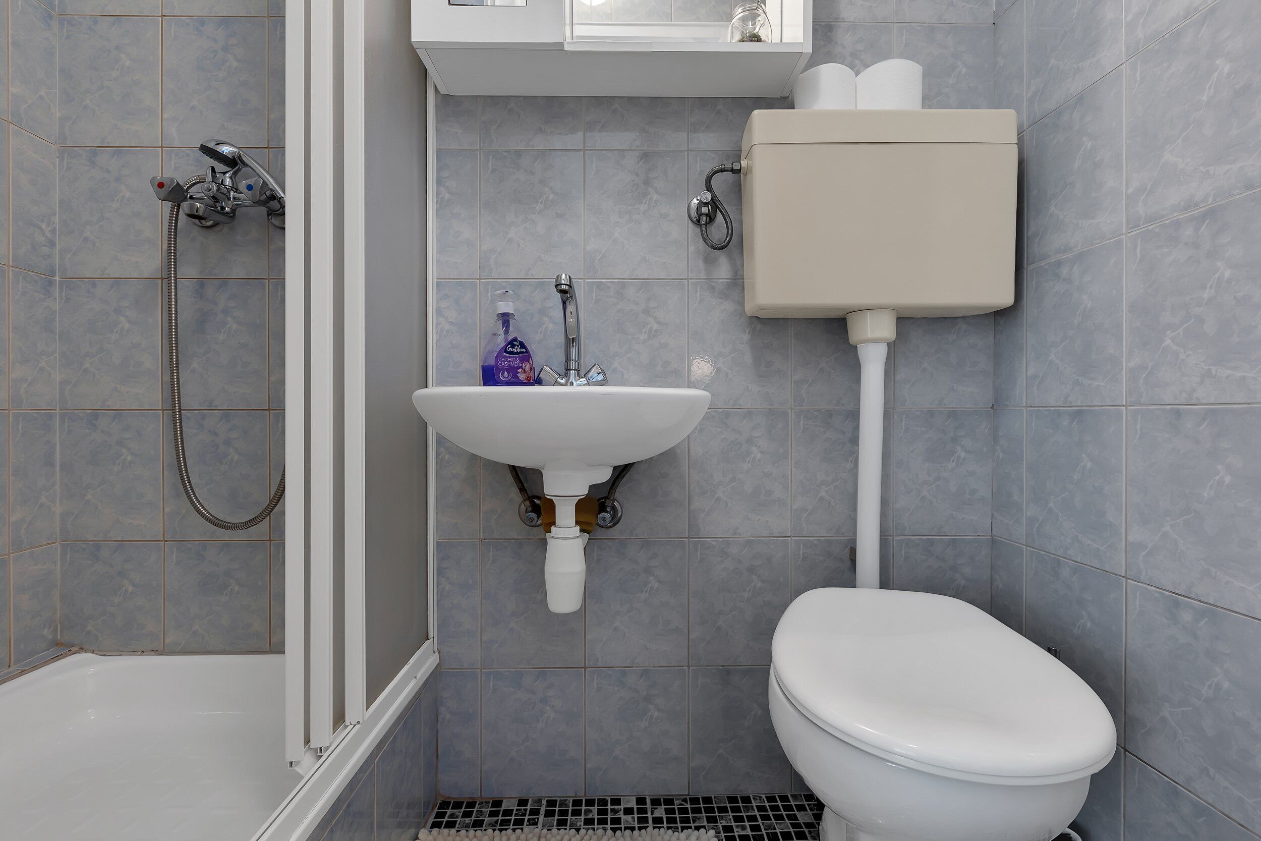 A bathroom with a shower, sink, toilet, and a toilet paper holder.