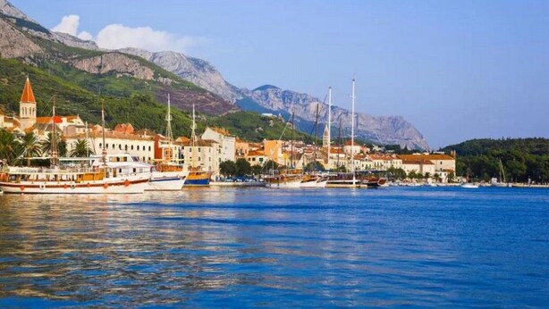 A coastal town with a marina, buildings with red roofs, and mountains in the background. - Apartments Kata (Makarska)