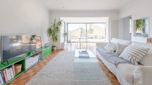 A modern living room with a flat-screen TV, a green entertainment unit, a white sofa, and a large window offering a view of the outdoors. - Peaceful 2 Bedroom Flat With Roof Terrace - Hackney (London)