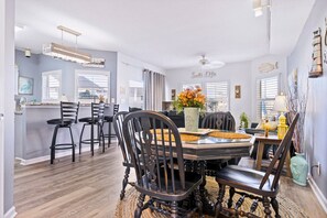 A dining area with a round table, black chairs, and a vase with flowers. - Hook, Wine, & Linger 2 Bedroom Condo by RedAwning (Destin)