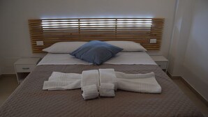 A neatly made bed with a wooden headboard, white and blue pillows, and folded white towels on the bed. - Brand new apartment and strategically located. (Terrasini)