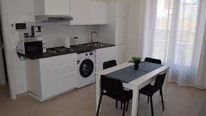 A compact kitchen with a microwave, stove, sink, and washing machine. There is a dining table with chairs and a potted plant. - Brand new apartment and strategically located. (Terrasini)
