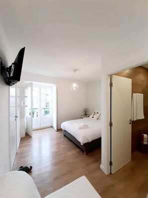 A bedroom with a bed, a TV mounted on the wall, and a door leading to a balcony. - Beautiful Family Apartment in Leiria (Leiria)