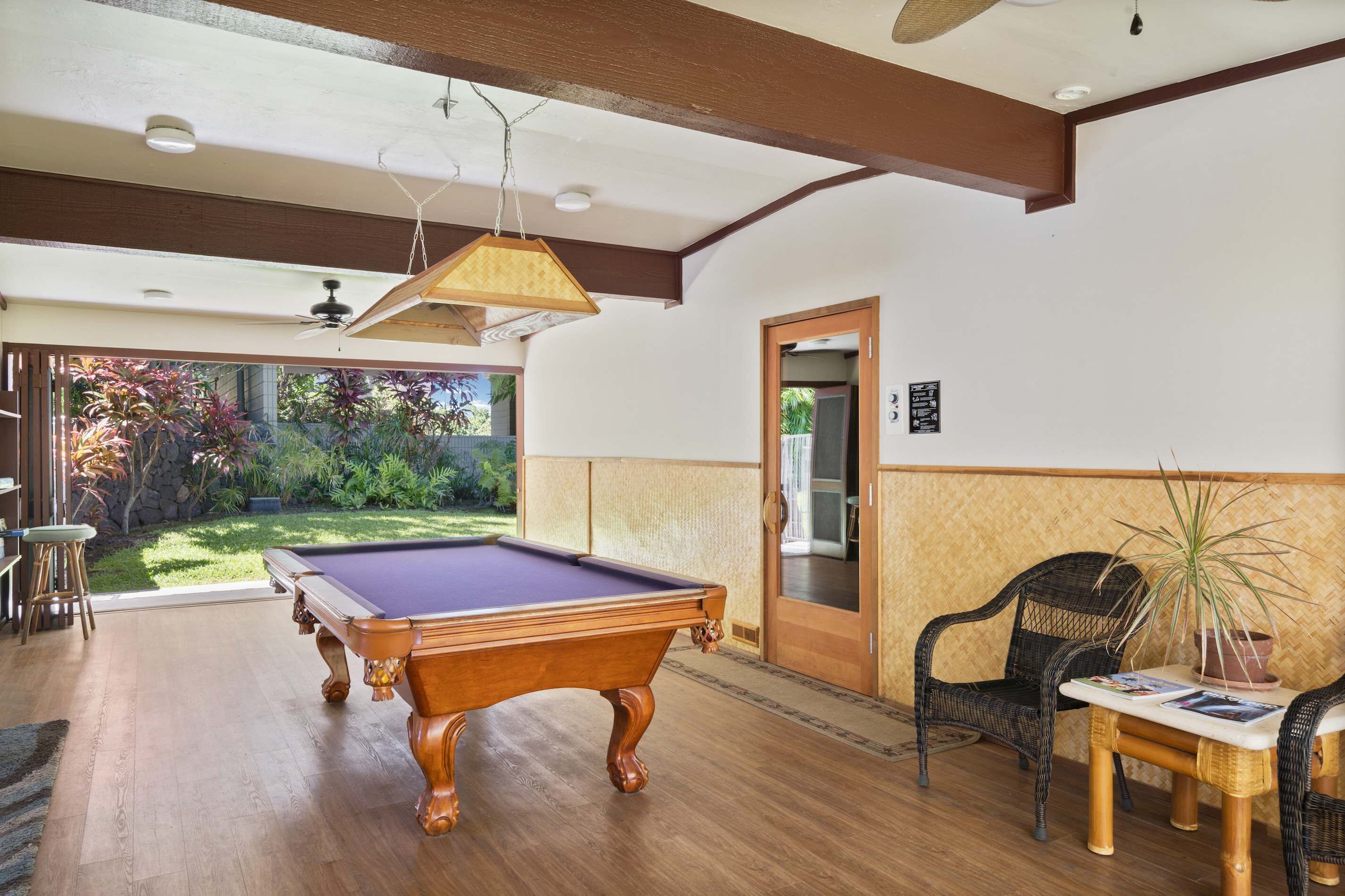 A pool table in a room with wooden flooring, a ceiling fan, and a door leading outside.