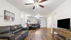A living room with a brown leather sofa, a wooden coffee table, a TV on a wooden stand, and a ceiling fan. - Abby's Place - Close to Attractions (Branson)