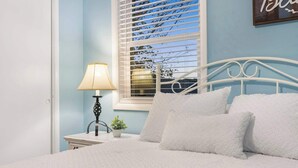 A bedroom with a white bed, white pillows, a bedside table with a lamp, and a window with blinds. - Abby's Place - Close to Attractions (Branson)