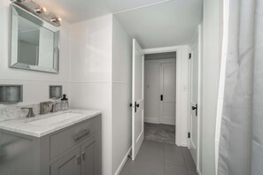 Un baño con tocador blanco, un espejo grande y zona de ducha.