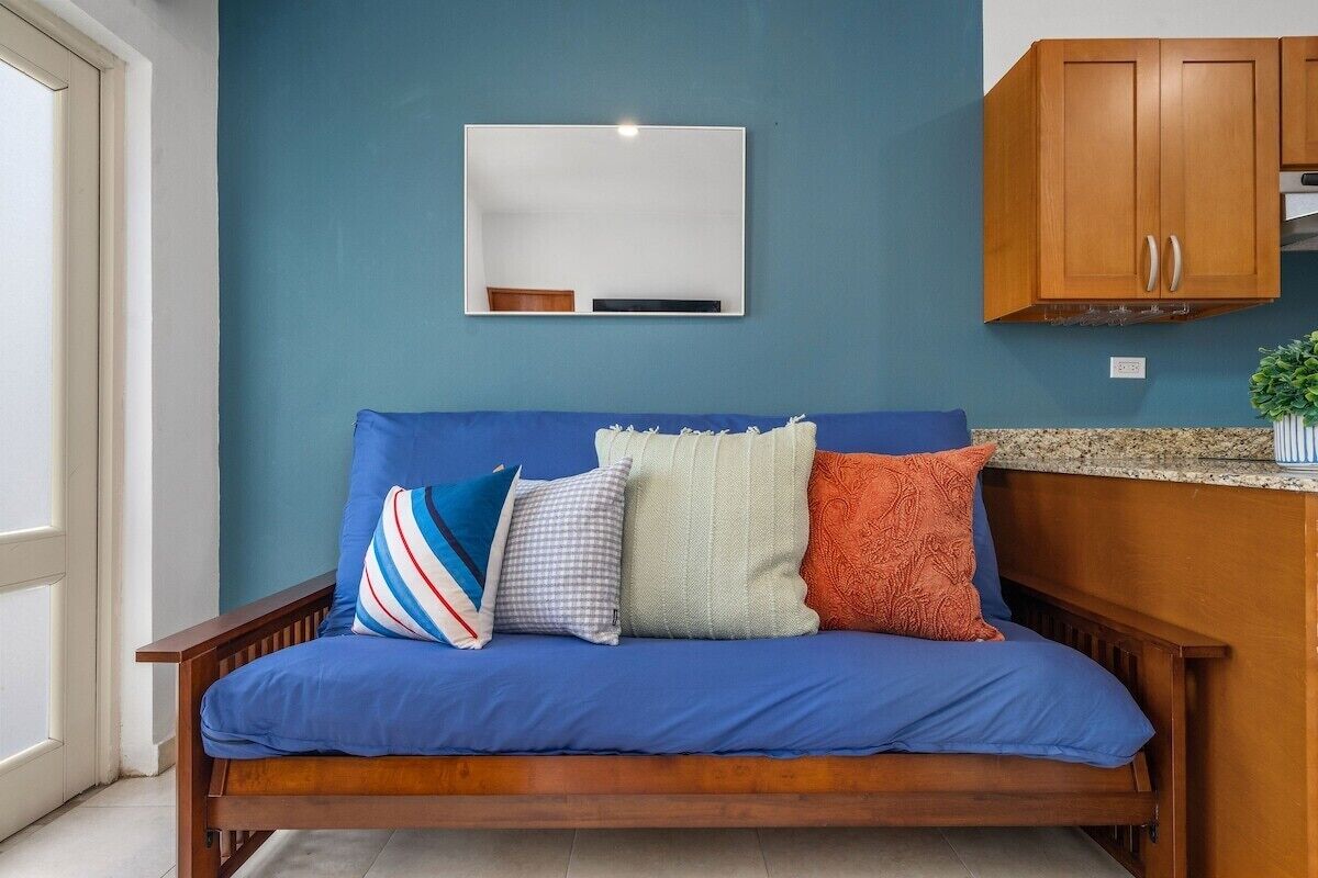 Un sofá azul con cuatro almohadones, un espejo blanco montado en la pared y armarios de madera en una habitación con una pared azul de acento.