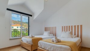 Een slaapkamer met twee bedden, een groot raam en uitzicht op gebouwen.