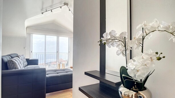 Een moderne woonkamer met een donkere bank, een klein tafeltje en een groot raam met uitzicht op gebouwen.