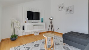 Een moderne woonkamer met een flatscreen-tv, een statieflamp, een donkere bank, een potorkidee en een vloerkleed met dessin.