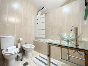 A modern bathroom with a toilet, bidet, glass sink, and a shower area.