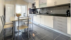 Een moderne keuken met een eethoek, met een zwart betegelde vloer, witte kasten en een hangende lamp.