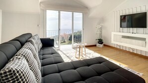 Een moderne woonkamer met een zwarte modulaire bank, een flatscreen televisie aan een witte muur en een balkon met uitzicht op de stad.