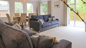 Ein modernes Wohnzimmer mit einer grauen Couch, einem Essbereich mit Stühlen und einem großen Fenster mit Blick ins Freie.