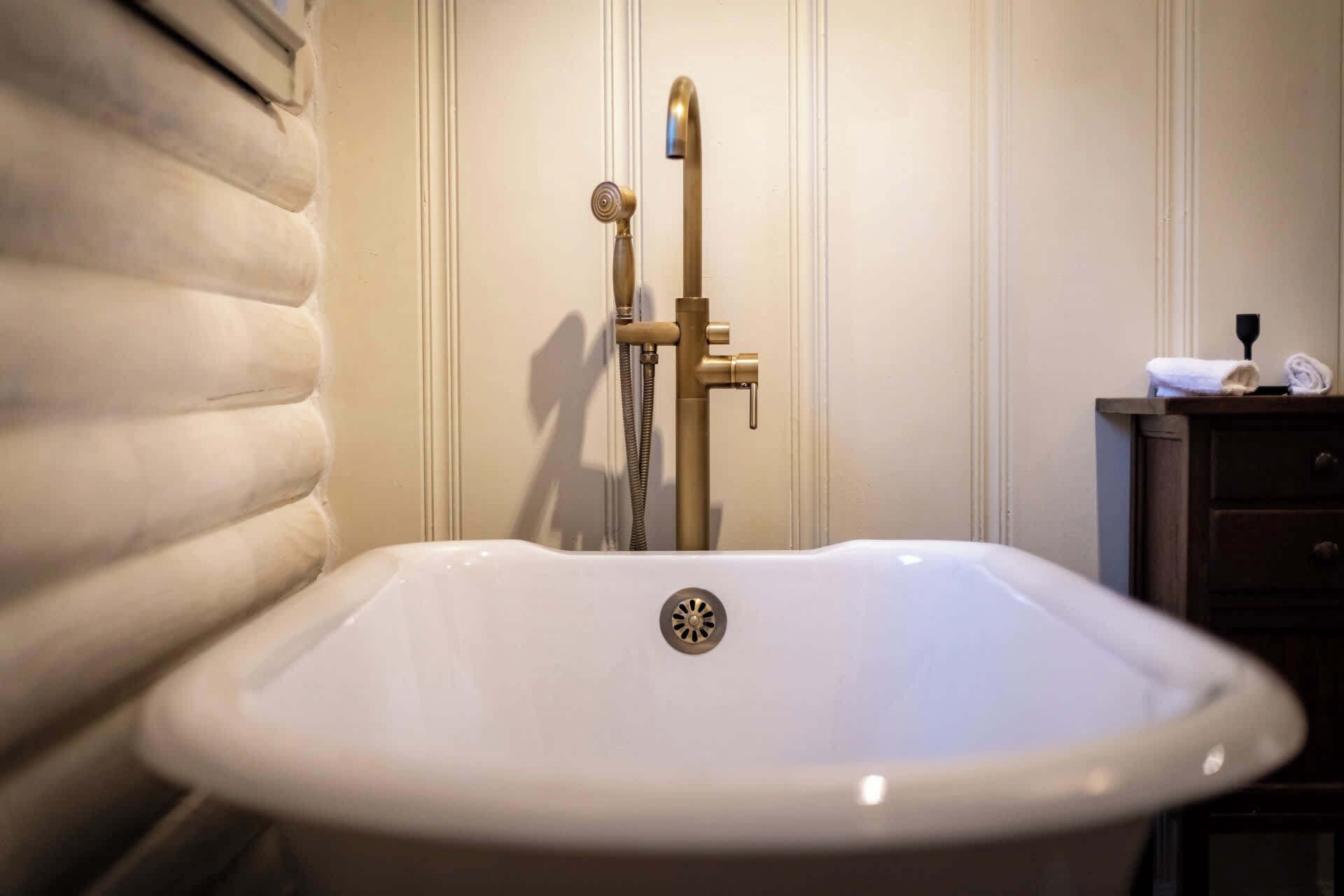 Un baño con una bañera blanca, un grifo dorado y un armario de madera con una toalla.