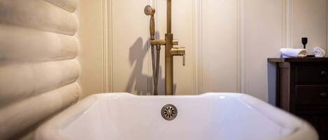 Un baño con una bañera blanca, un grifo dorado y un armario de madera con una toalla.