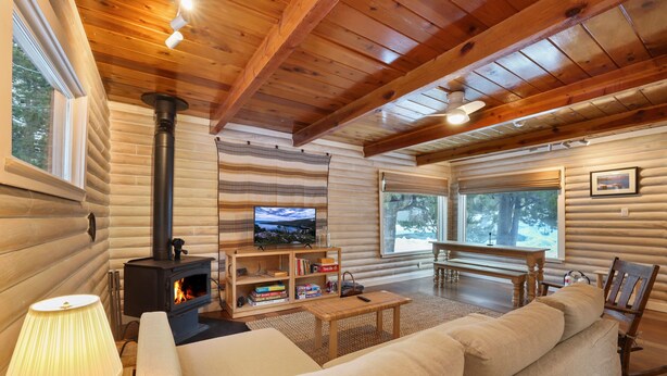 L’intérieur d’une cabane en rondins, avec une cheminée, un canapé, une télévision et des meubles en bois.