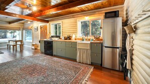 Une cuisine rustique aménagée dans une cabane en rondins, avec des poutres en bois, un réfrigérateur en acier inoxydable et une grande fenêtre donnant sur la forêt.