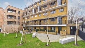 A multi-story residential building with balconies, a paved courtyard, and young trees. - Greenwich Perfection (London)