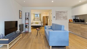 A modern living room with a TV, sofa, and a small table. A bunk bed is visible in the background. - Greenwich Perfection (London)