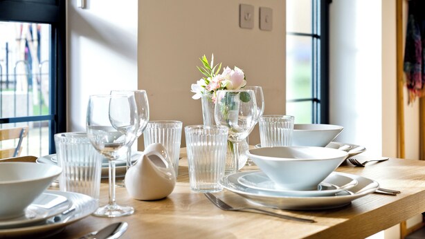 A dining table set with clear glassware, white plates, and a vase with flowers. - Greenwich Perfection (London)