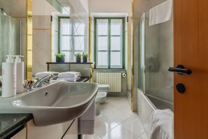 A modern bathroom with a large sink, toilet, and shower. There are plants on the windowsill and towels on the counter.