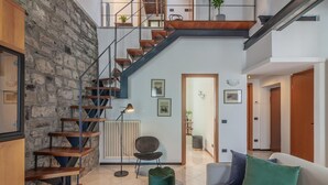 Un soggiorno moderno con una scala in legno, un divano, un pouf verde e un termosifone.
