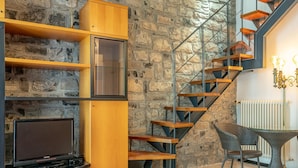 Un interno moderno con una parete in pietra, una scala in legno e una zona pranzo con mobili in vimini.