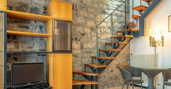 A modern interior with a stone wall, wooden staircase, and a dining area with wicker furniture.
