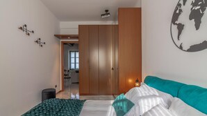 Una camera da letto con un letto, un divano color petrolio, un'opera d'arte a tema globo e un armadio in legno.