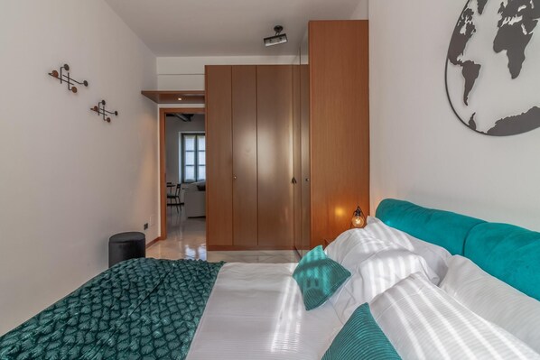 A bedroom with a bed, a teal sofa, a globe wall art, and a wooden wardrobe. - Bellagio Central Square by Wonderful Italy (Bellagio)