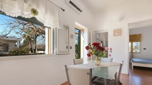 Una habitación moderna con una mesa de vidrio para comer, una cama y una ventana que ofrece vistas a árboles y un edificio.