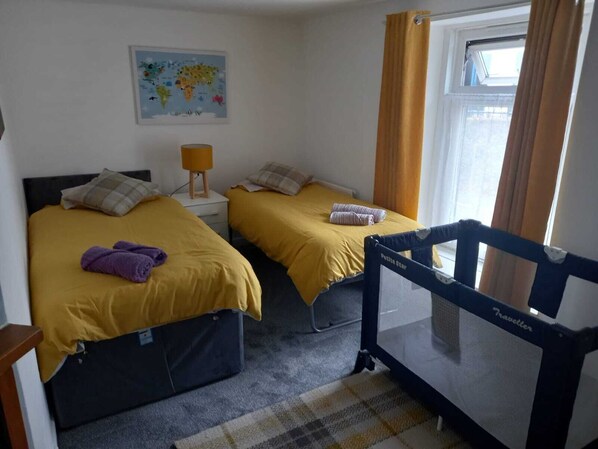 A room with two beds, a map on the wall, a window with curtains, and a crib labeled 'Traveller'. - Cosy Cottage, a Spacious Home in Torquay (Torquay)