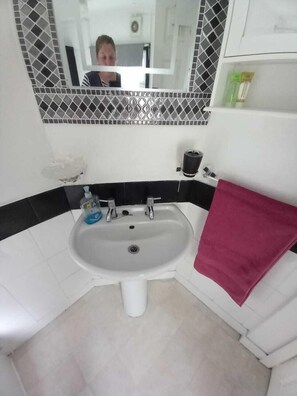 A bathroom with a white sink, black and white tiled backsplash, a mirror, and a red towel. - Cosy Cottage, a Spacious Home in Torquay (Torquay)