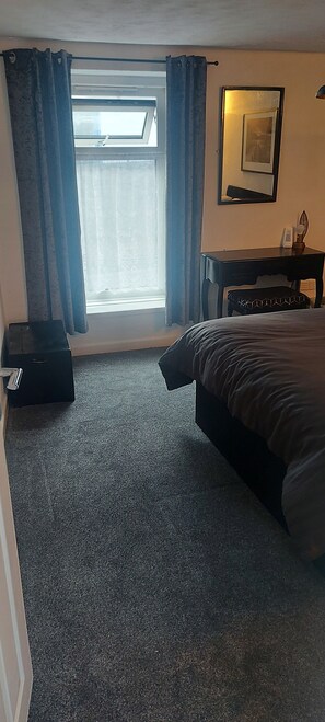 A bedroom with a bed, a desk, a chair, a small table with a lamp, and a window with curtains. - Cosy Cottage, a Spacious Home in Torquay (Torquay)