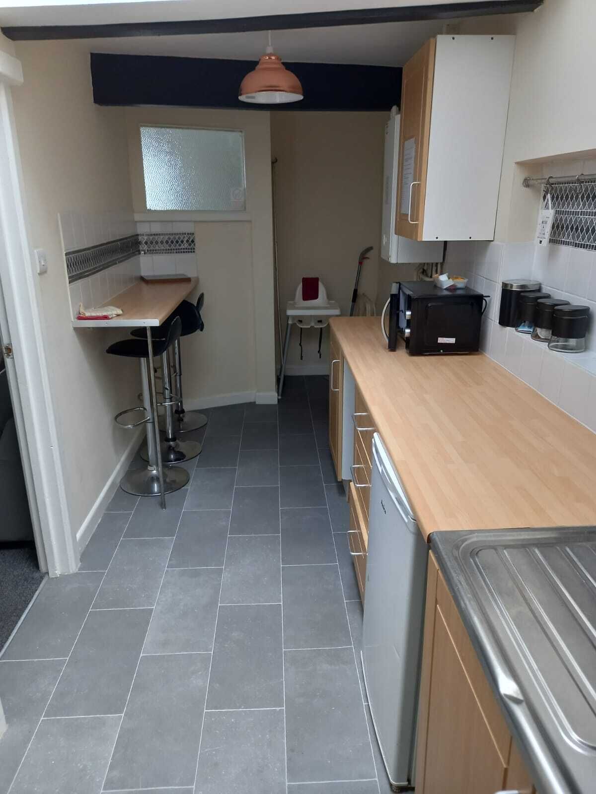 Cocina compacta con encimera de madera, un lavamanos y una estufa. Hay un pequeño comedor con una mesa y sillas.