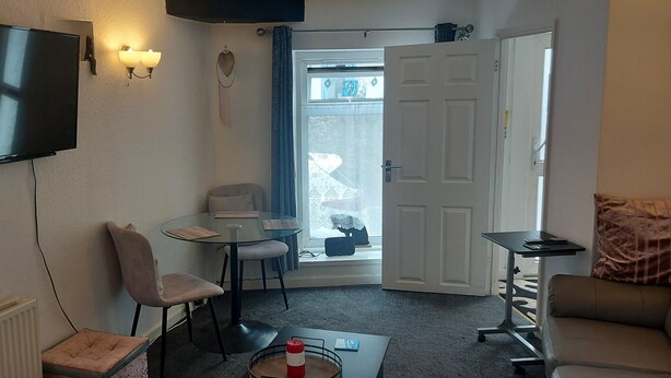Ein kompakter Wohnbereich mit einem an der Wand befestigten Flachbildfernseher, einem kleinen runden Tisch mit zwei Stühlen, einer Couch und einer Tür zu einem Balkon.